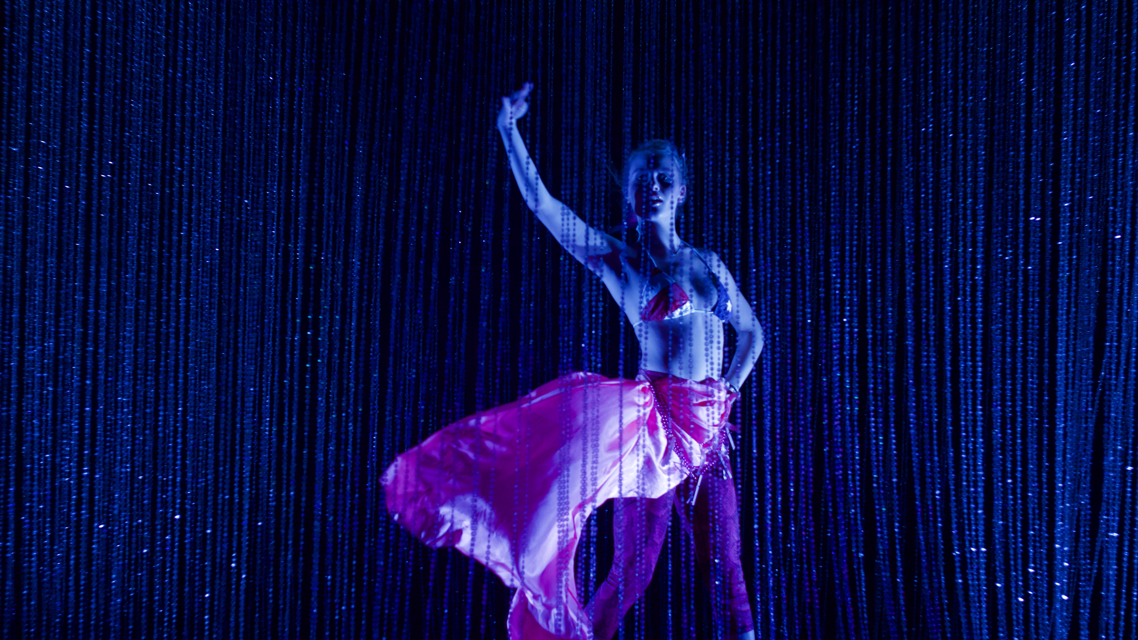 A photo of a woman wearing a mermaid costume behind a blue bead curtain